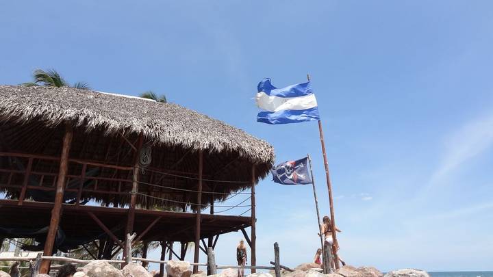 Nicaraguan flags on a beach with a thatched building.