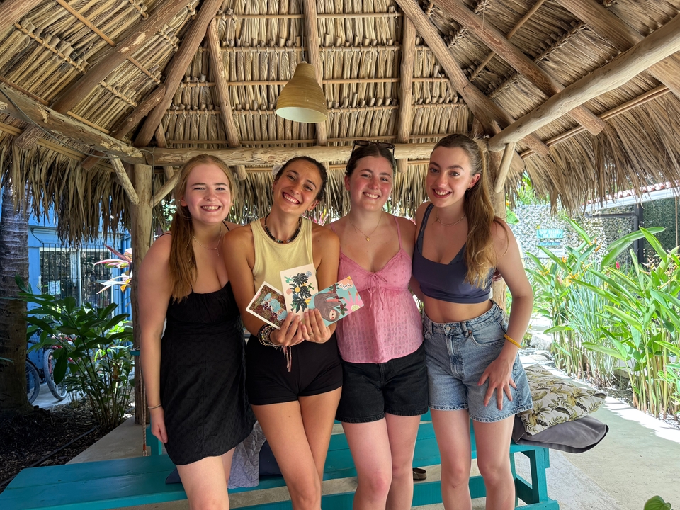 Quatre amis posant sous une hutte au toit de chaume dans un jardin tropical.