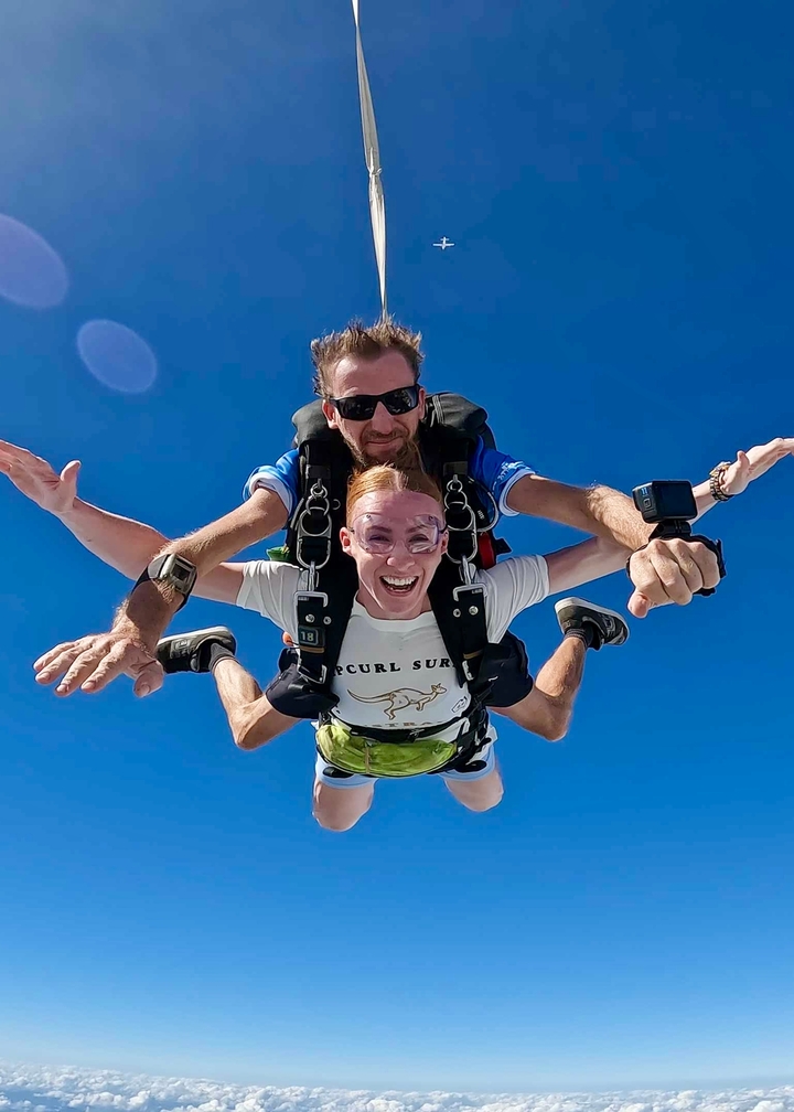 Parachutistes en tandem en chute libre, souriant à la caméra.