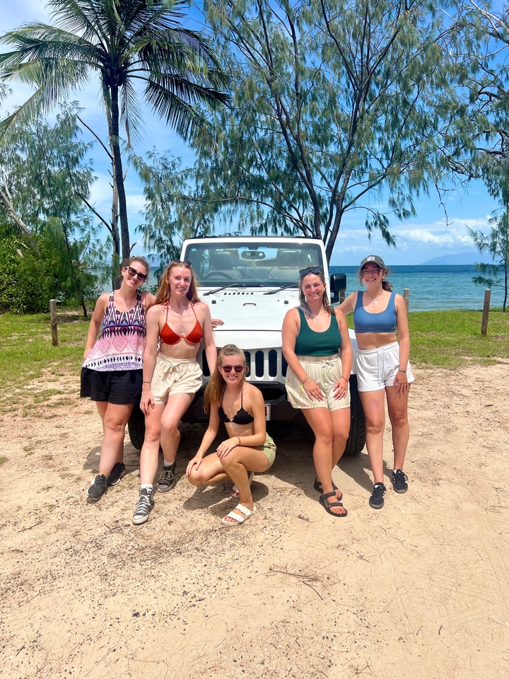 Des femmes posent devant une jeep sur la plage.