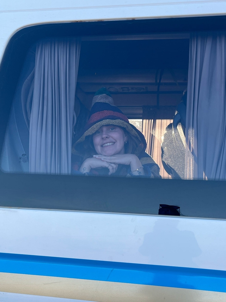 Person, die durch ein Fenster mit Vorhängen lächelt.