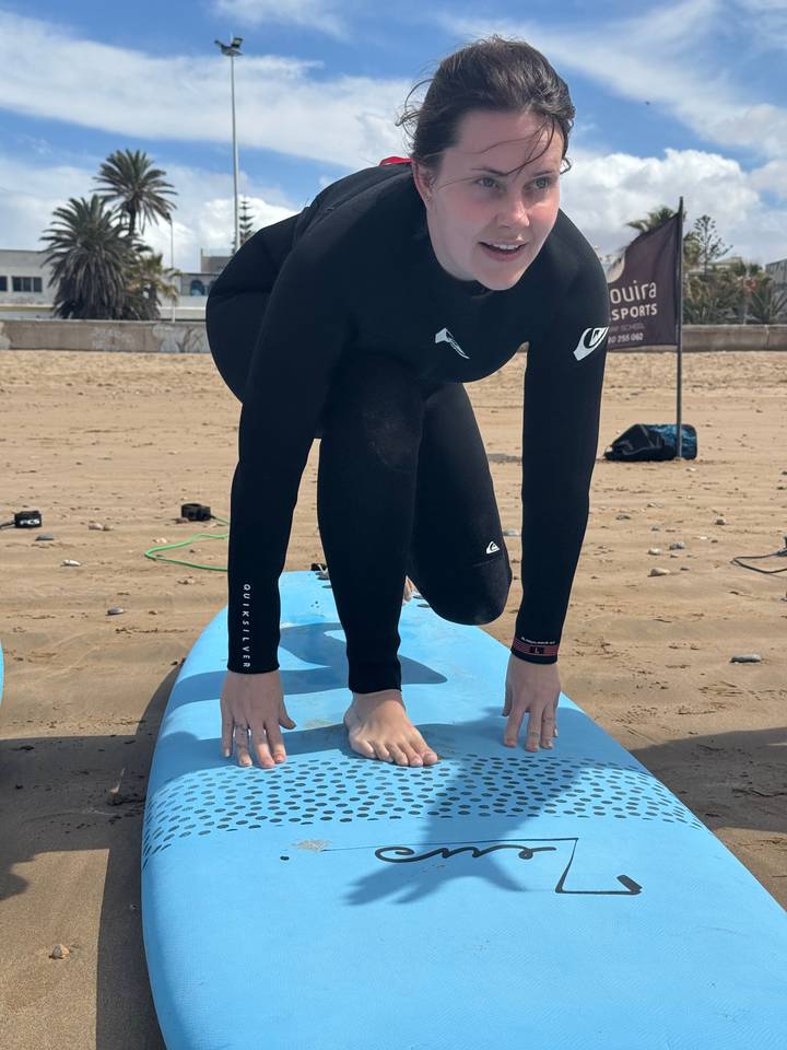 Person in einem Neoprenanzug, die auf einem Surfbrett kniet.