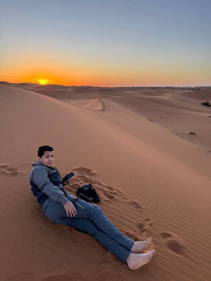 Person, die bei Sonnenuntergang auf einer Sanddüne sitzt.
