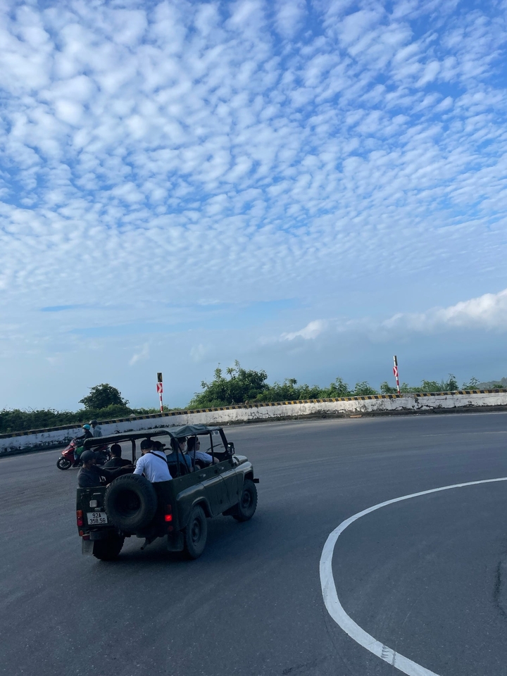 Des gens dans des véhicules sur une route sinueuse sous un ciel clair.