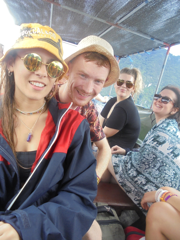 Friends smiling on an open-air boat with jungle-covered hills behind them.