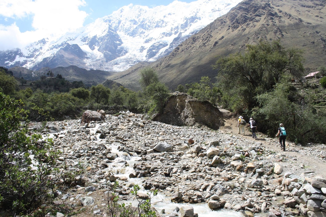 Randonneurs marchant sur un sentier de montagne aux sommets enneigés.