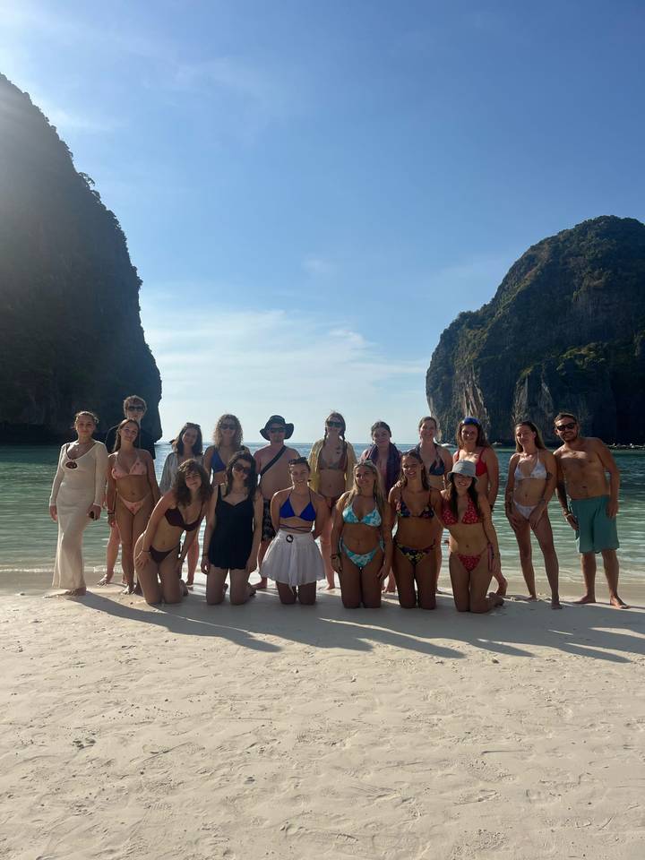 Groupe de personnes sur une plage avec des formations rocheuses en arrière-plan.