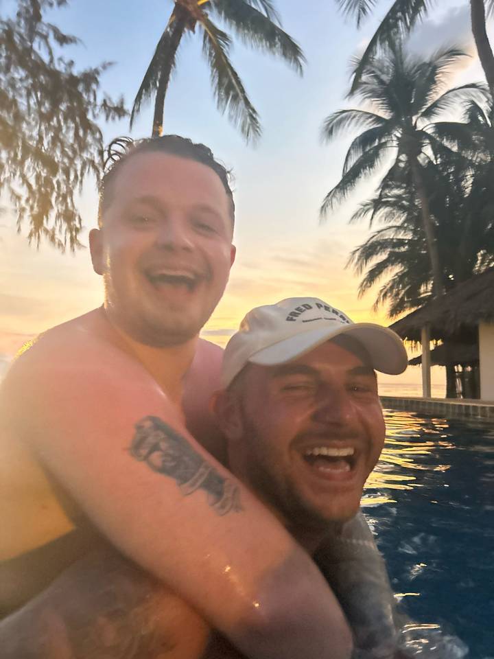 Deux personnes souriantes avec un coucher de soleil et une piscine en arrière-plan.
