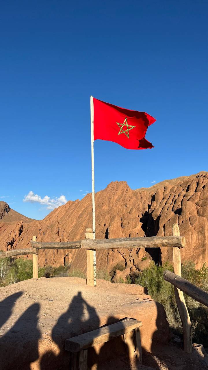 Eine rote marokkanische Flagge an einem Mast mit zerklüfteten Bergen im Hintergrund.
