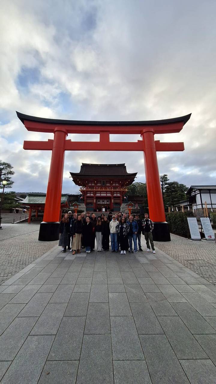 Groupe de personnes posant devant un sanctuaire japonais avec de grands piliers rouges.