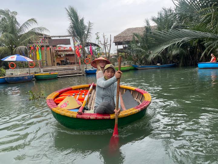 Femme ramant dans un bateau-panier près du rivage avec des huttes.