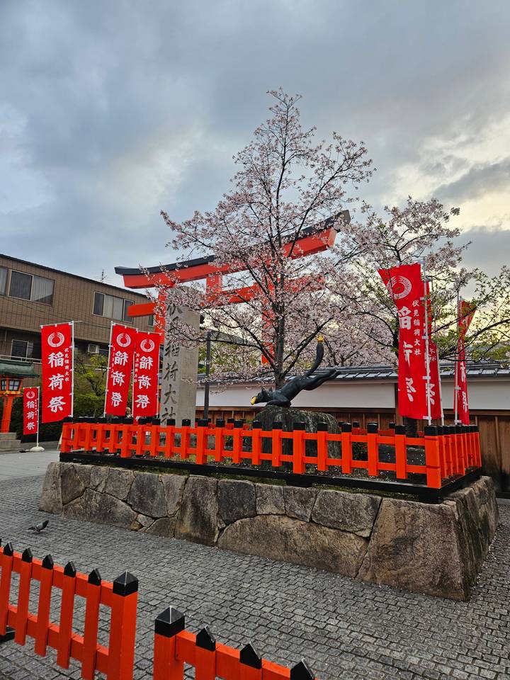 Une porte torii avec des fleurs de cerisier et des bannières rouges.