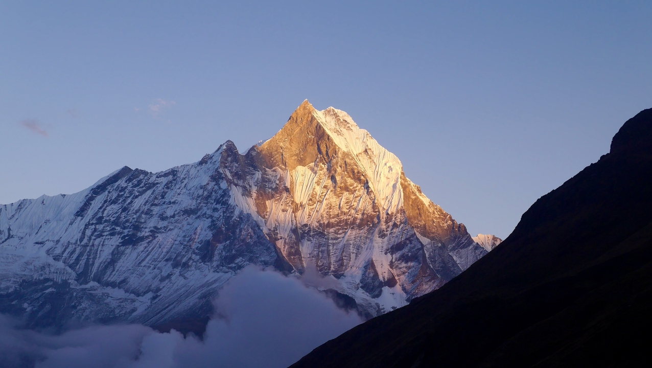 Coucher de soleil sur un pic montagneux enneigé avec des nuages en contrebas.