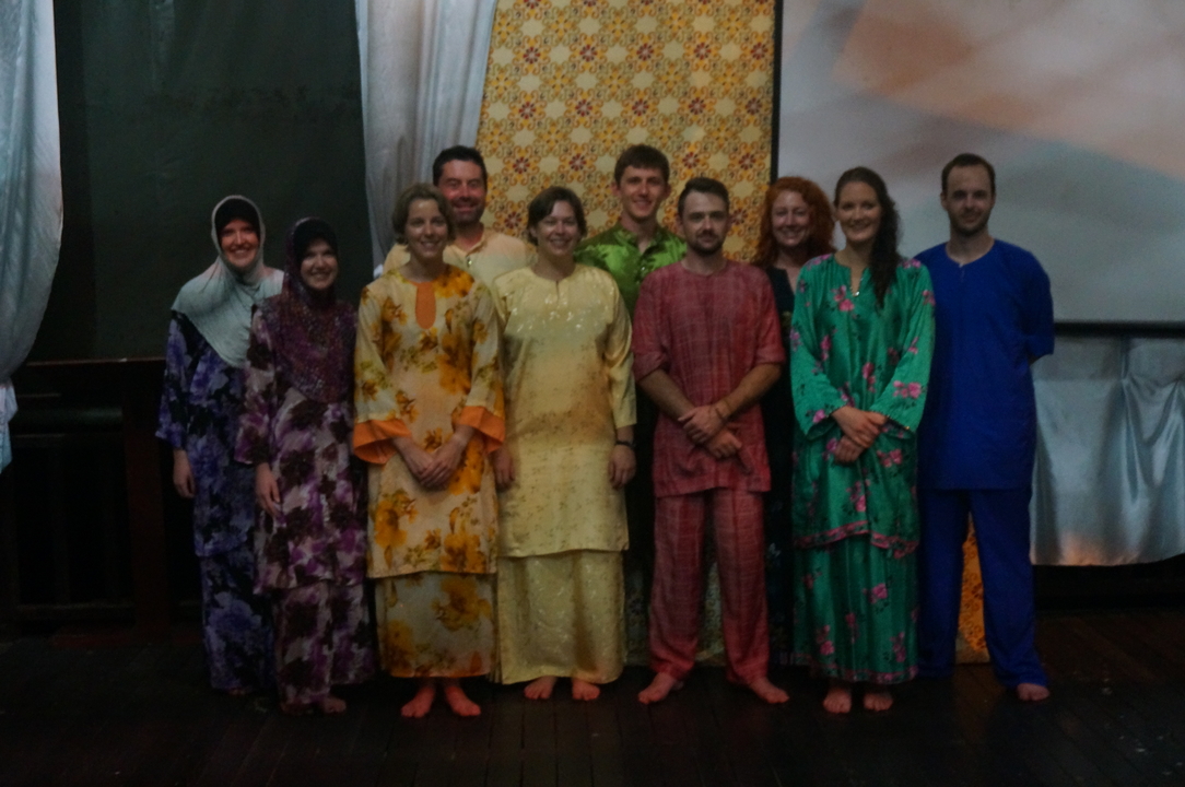 Groupe de personnes portant des vêtements traditionnels posant dans une pièce faiblement éclairée.