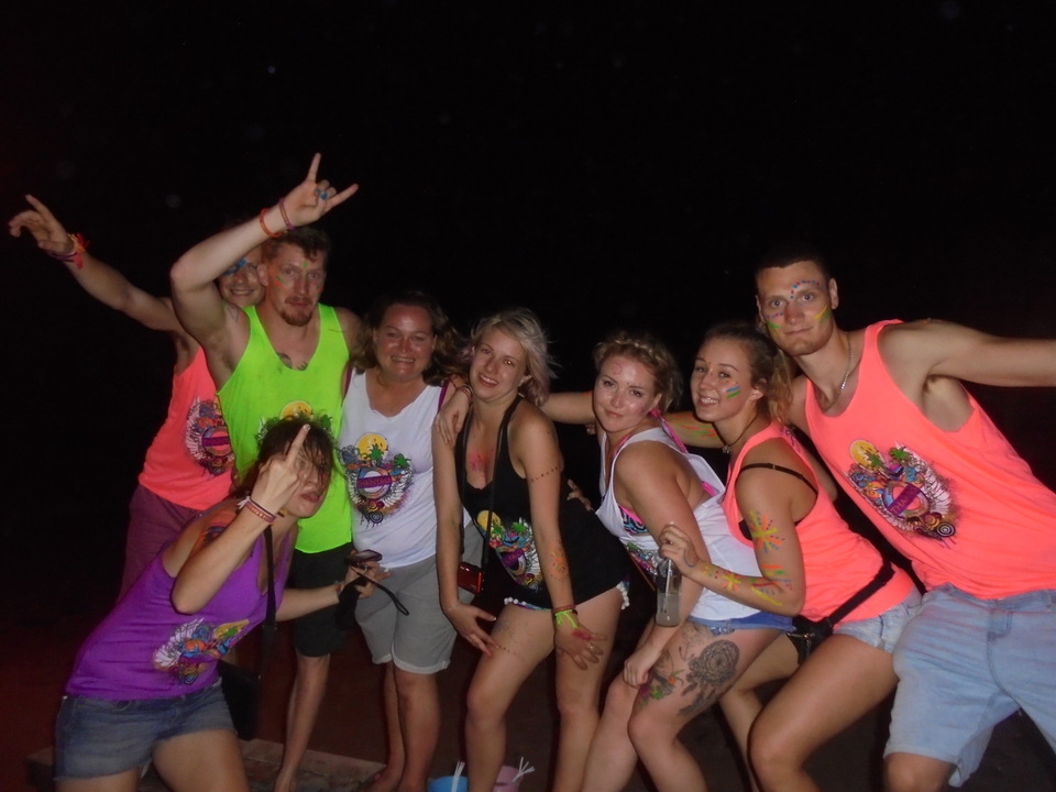 Group of people at a beach party at night with neon paint on shirts.