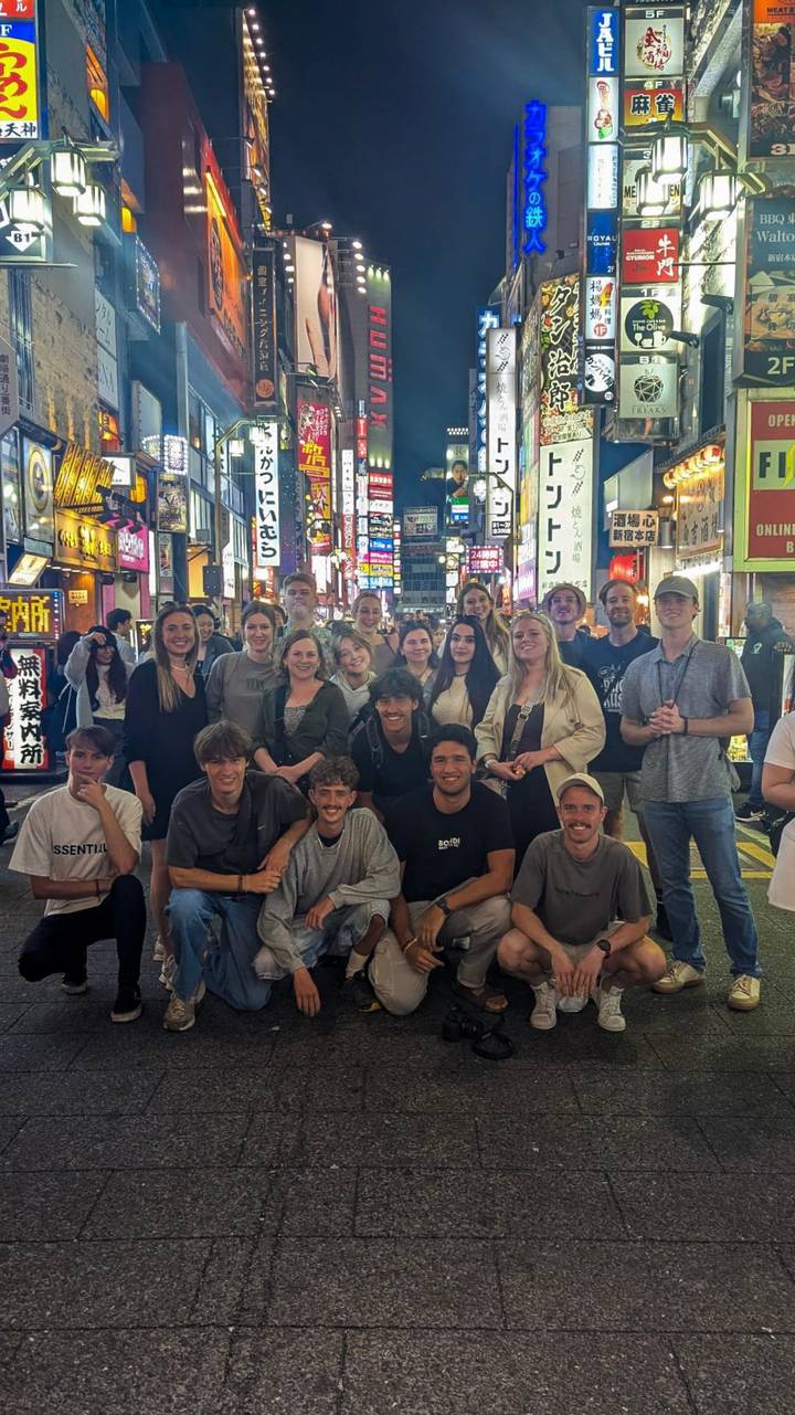 Un groupe de personnes posant dans une rue de ville animée remplie de néons.