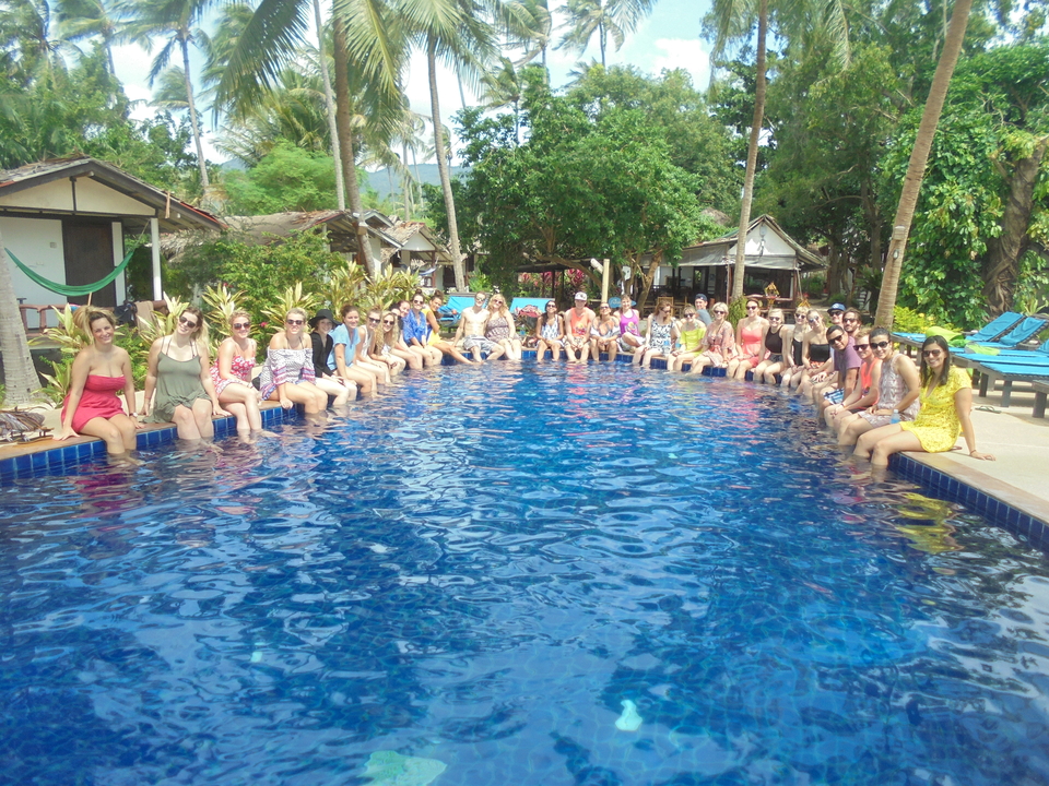 People seated around a large pool in a lush setting.
