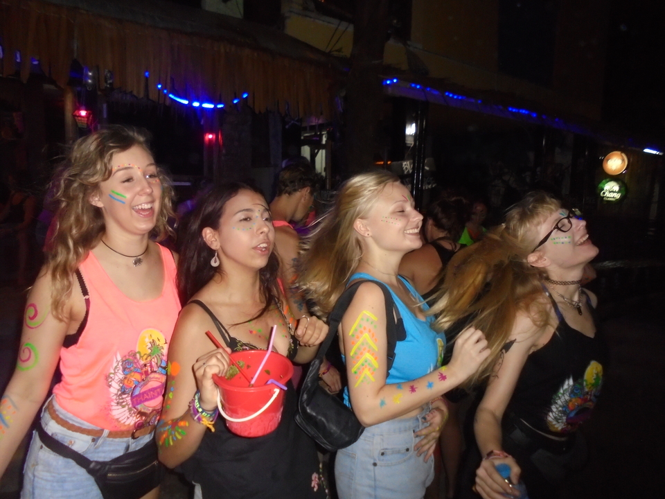 Women enjoying a colorful party with face paint and lights.