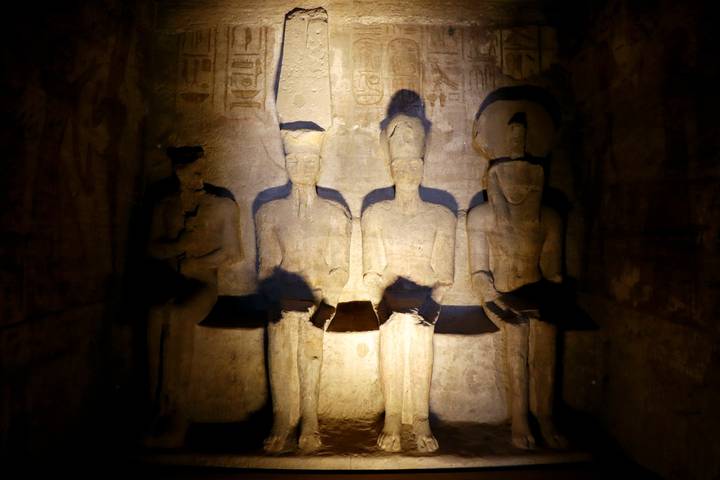 Statues of seated figures inside a dimly lit ancient Egyptian temple.