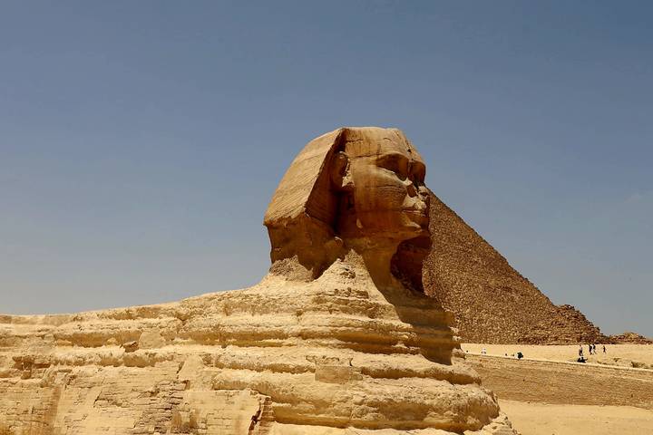 The Sphinx with a pyramid in the background under a clear sky.