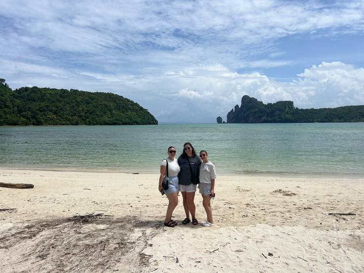 Trois personnes debout sur une plage avec des îlots rocheux en arrière-plan.
