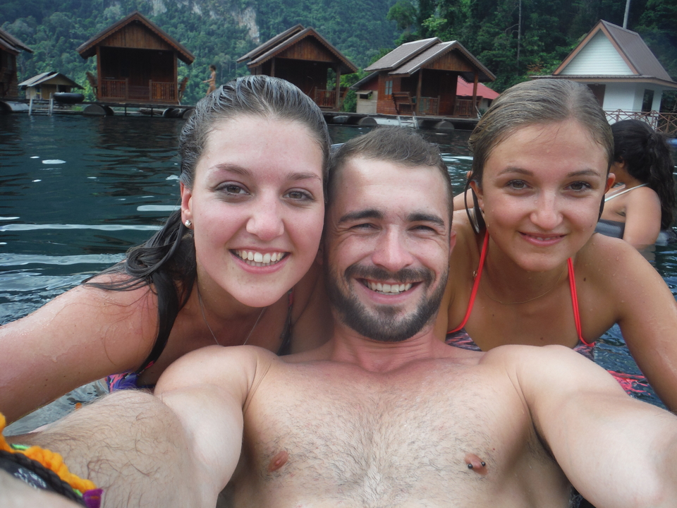 Trio smiling while in water with floating houses in the background.