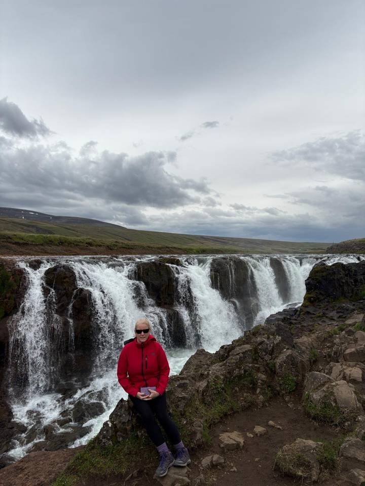 Homme devant une cascade pittoresque sous un ciel nuageux.