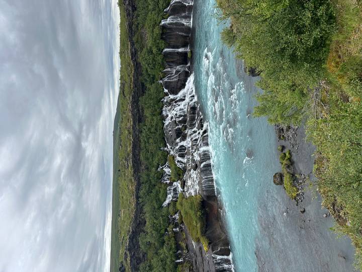 Belle cascade avec eau turquoise entourée de feuillage vert.