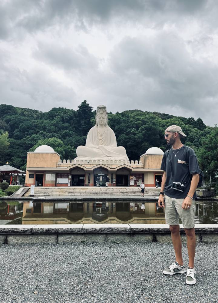 Personne à côté d'une grande statue de Bouddha entourée par la nature.