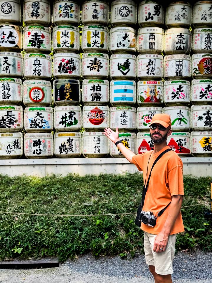 Personne pointant vers des tonneaux de saké décorés empilés à l'extérieur.