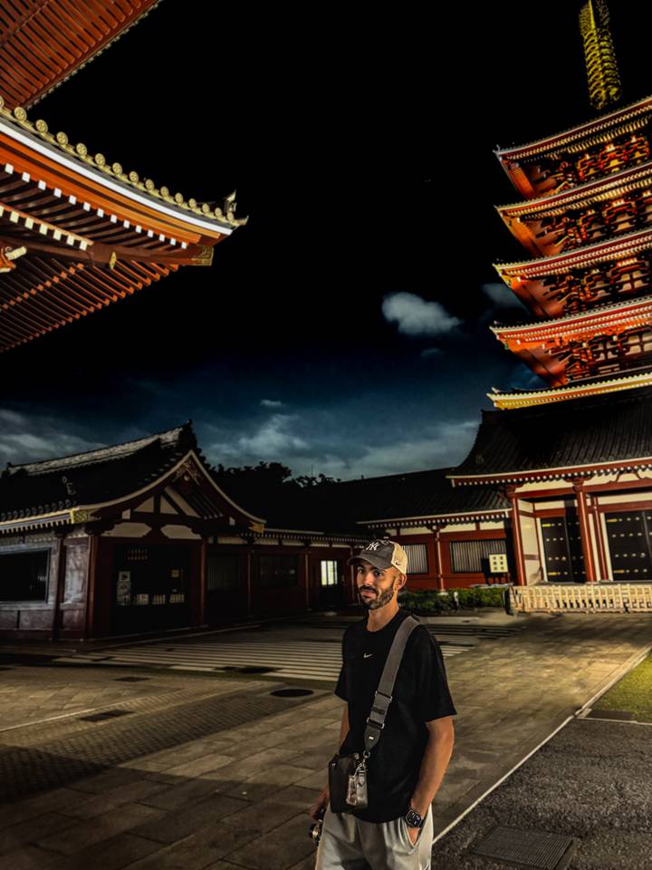 Personne debout devant des bâtiments de temple illuminés la nuit.