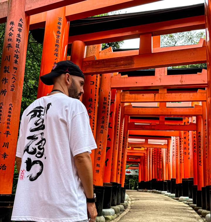 Homme parmi des rangées de torii rouges.