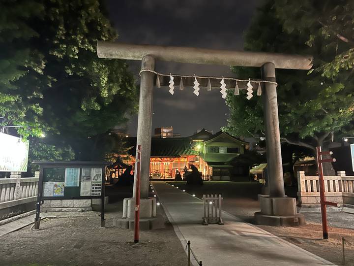 Un portique torii à l'entrée d'un complexe de sanctuaire la nuit.