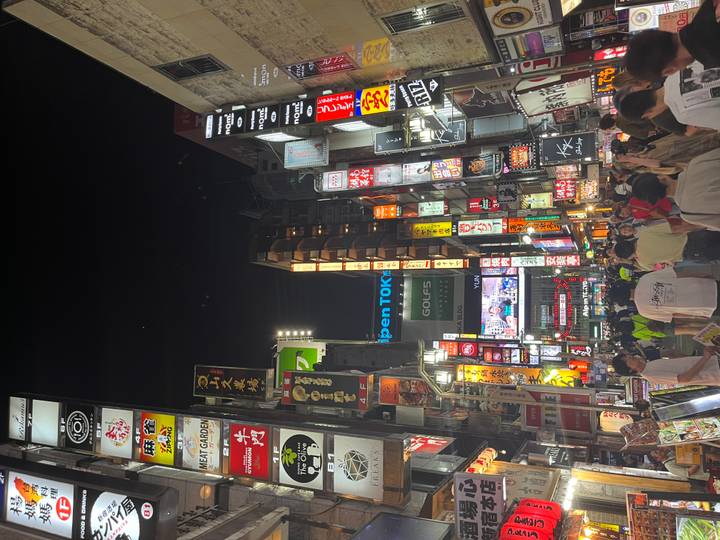Rue animée la nuit avec des enseignes illuminées et des gens.