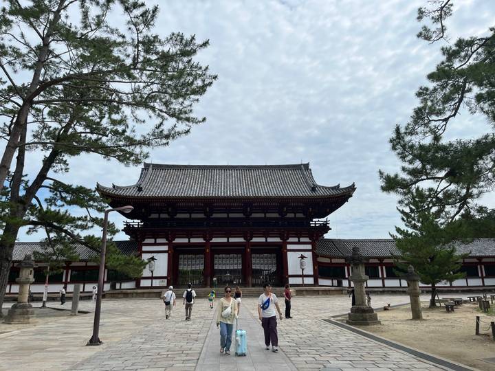 Une grande structure traditionnelle entourée d'arbres et de gens.
