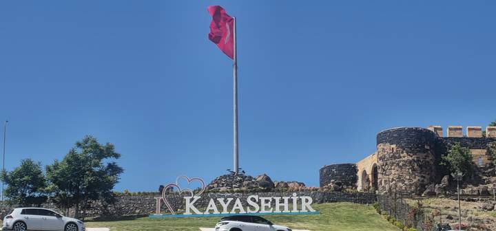 Panneau et mât avec drapeau turc et structure en pierre en arrière-plan.