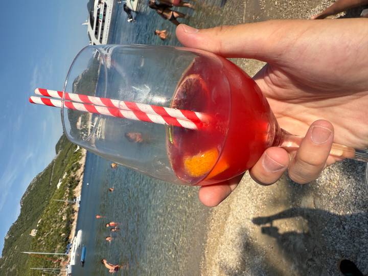 Main tenant un verre de cocktail avec une plage en arrière-plan.