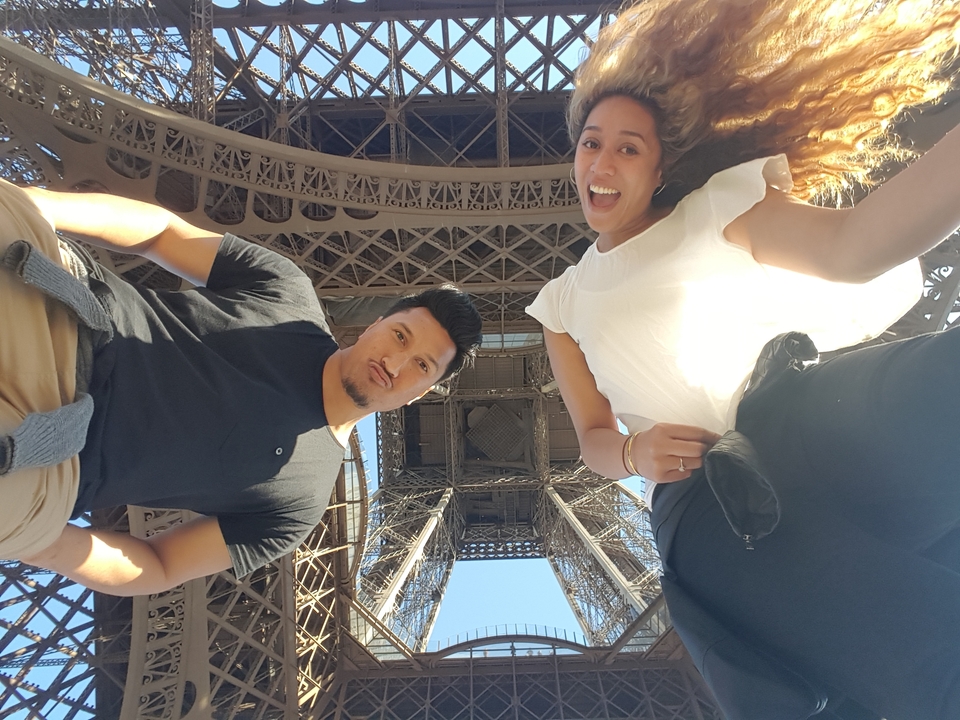 Couple taking a playful selfie beneath the lattice ironwork of the Eiffel Tower.