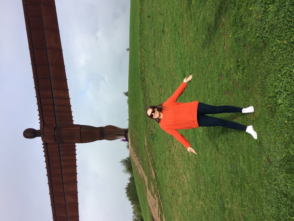 Une femme pose les bras ouverts devant une grande sculpture.