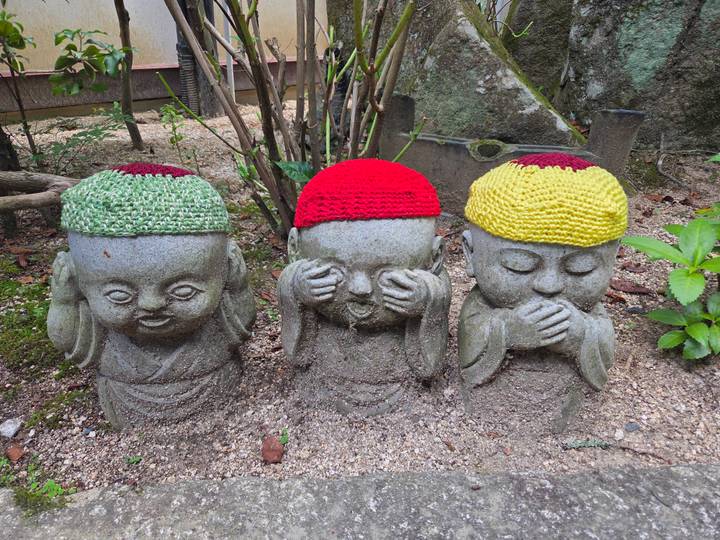 Trois statues de pierre avec des bonnets tricotés colorés.