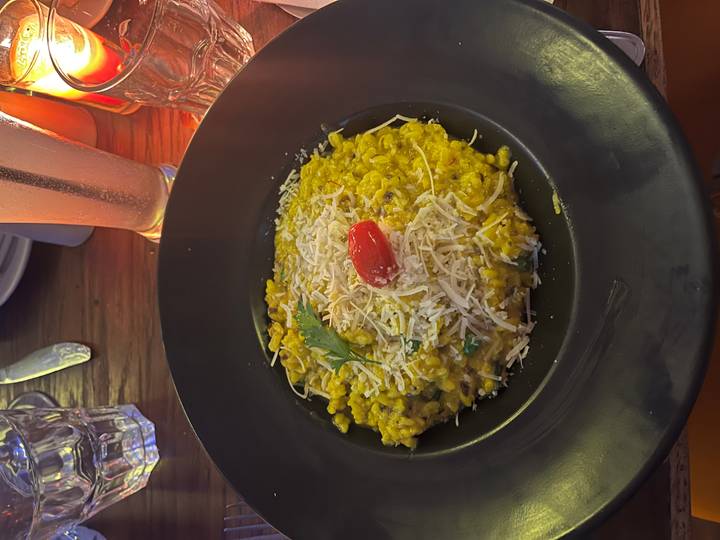 Cremiges gelbes Risotto garniert mit einer roten Kirschtomate und Käse.