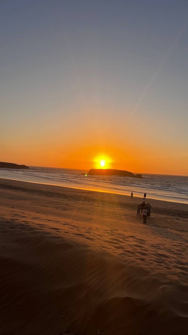 Sonnenuntergang am Strand mit Silhouetten von Menschen und einem orangefarbenen Himmel.