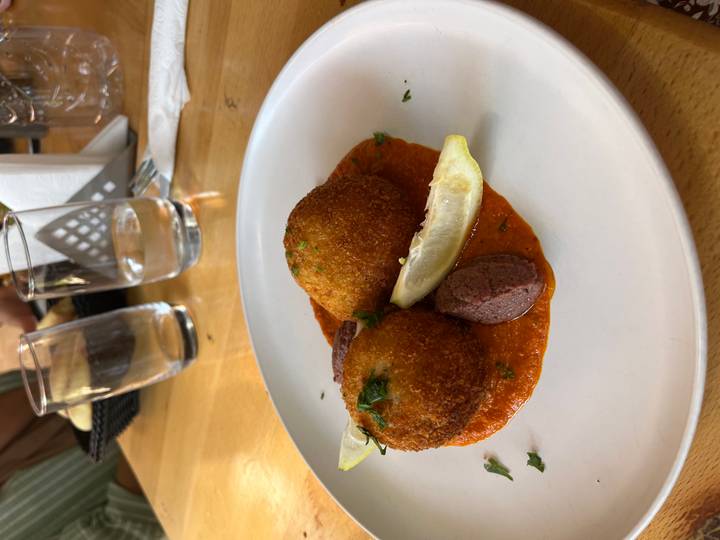 Zwei frittierte Kroketten angerichtet mit Zitronenspalten und Sauce.