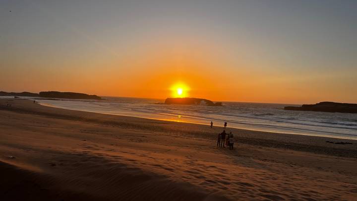 Sonnenuntergangsblick auf einen Strand mit Silhouetten von Menschen in der Ferne.