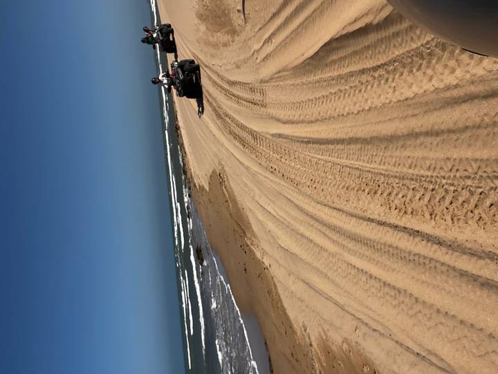 Person, die ein Quad am Strand fährt mit sichtbaren Reifenspuren.