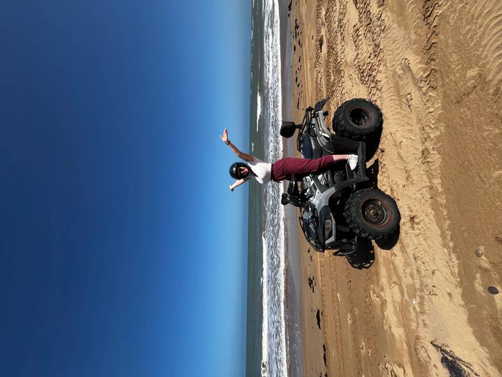 Frau steht auf einem ATV und posiert am Strand mit erhobenen Armen.