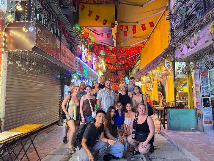 Groupe de personnes posant dans une rue colorée et animée avec des enseignes illuminées.