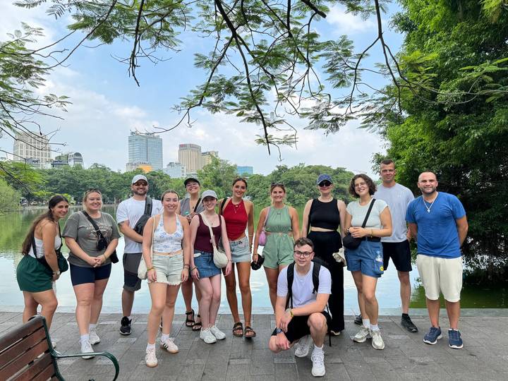 Groupe de personnes posant près d'un lac avec des arbres et des bâtiments en arrière-plan.