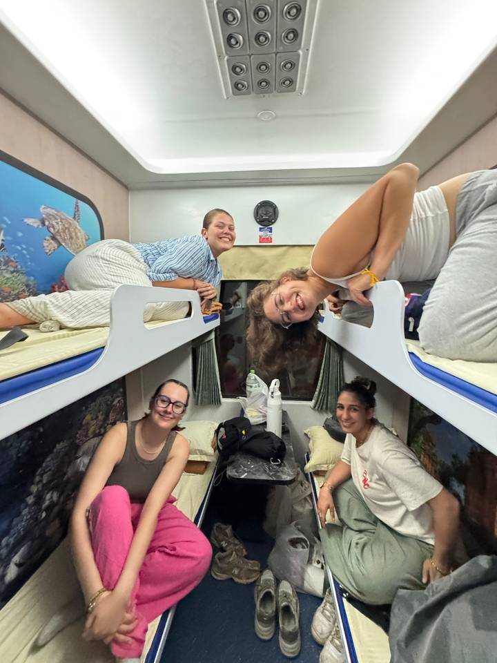 Quatre personnes assises dans un compartiment de train avec des lits superposés.