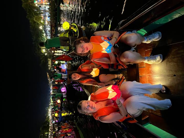 Des gens dans un bateau tenant des lanternes sur une rivière la nuit.